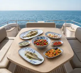 Ahşap tekne masasında ızgara balık, paella, meze ve salata ikramlarıyla sunulan mavi yaprak motifli kırılmaz melamin 7 parça Selva Blue (501407) kayık sunum seti.