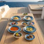 Ahşap tekne masasında çorba, balık, makarna, meze ve salata ikramlarıyla sunulan canlı mavi iris reaktif sir efektli kırılmaz melamin 16 parça Blue Iris (504216) yemek takımı seti.
