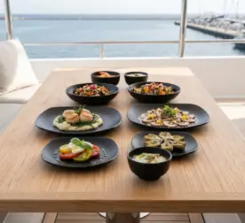 Ahşap tekne masasında deniz tarağı, ızgara ahtapot, caprese salatası ve enginar ikramlarıyla sunulan mat siyah döküm taş efektli kare kırılmaz melamin 8 parça Obsidian (M501208) 2 kişilik yemek takımı seti.