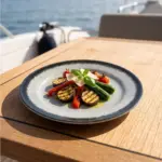 Ahşap tekne masasında ızgara patlıcan, kabak, kırmızı biber, çeri domates, parmesan dilimleri ve taze fesleğen yaprağı eşliğinde sunulan ızgara sebze tabağı sunumuyla gösterilen koyu kenarlı buz mavisi-gri çatlatmalı sır (crackle glaze) efektli kırılmaz melamin 3'lü büyük boy yuvarlak servis ve ana yemek tabağı seti (Ø 25 cm).