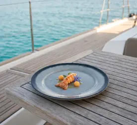 Turkuaz deniz manzaralı ahşap tekne güverte masasında böcek/istakoz kuyruğu (lobster tail) sunumu, gurme püre küreleri, yeşil ot sosu ve mor yenilebilir yıldız çiçeği eşliğinde gösterilen koyu kenarlı buz mavisi-gri çatlatmalı sır (crackle glaze) efektli kırılmaz melamin 3'lü ekstra büyük boy (battal) yuvarlak servis ve supla tabağı seti (Ø 28 cm).