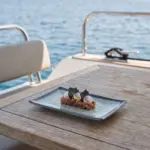 Ahşap tekne masasında turp dilimleri, siyah cipsler ve zeytinyağı sosu eşliğinde gurme ton balığı tartar sunumuyla gösterilen buz mavisi-gri çatlatmalı sır (crackle glaze) efektli kırılmaz melamin 6'lı dikdörtgen servis ve sunum tabağı seti (20 x 13,7 cm).