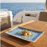 Ahşap tekne masasında yeşil pesto sos, taze mikro filizler ve sarı-mor yenilebilir çiçekler eşliğinde tavada mühürlenmiş deniz tarağı (scallops) ikramı sunumuyla gösterilen açık krem çerçeveli reaktif okyanus mavisi efektli kırılmaz melamin 3'lü büyük boy dikdörtgen servis ve sunum tepsisi seti (30 x 20,7 cm).
