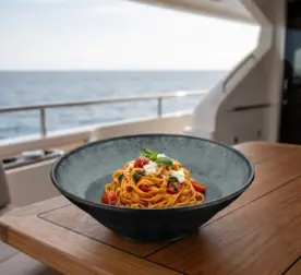 Ahşap tekne masasında domatesli ve fesleğenli fettuccine pasta sunumuyla gösterilen yeşil mineral reaktif taş efektli kırılmaz melamin Green Minerra 3'lü derin makarna ve salata kasesi seti (Ø 23,6 cm).